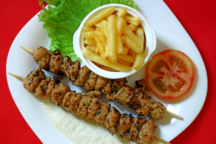 A white plate topped with kebabs and french fries